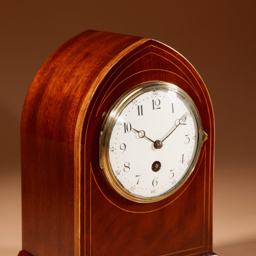 An Edwardian inlaid mahogany mantel clock with a lancet arch top, white enamel dial with Arabic numerals, and brass bun feet. View IV