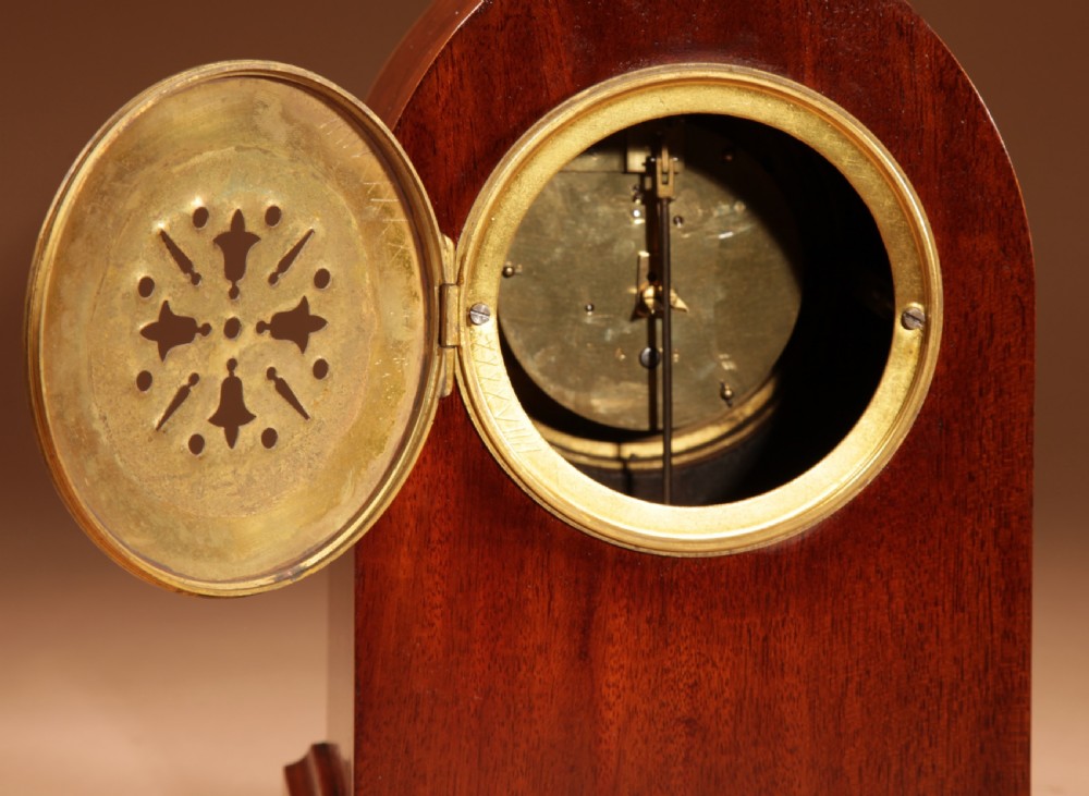 An Edwardian inlaid mahogany mantel clock with a lancet arch top, white enamel dial with Arabic numerals, and brass bun feet. View IX