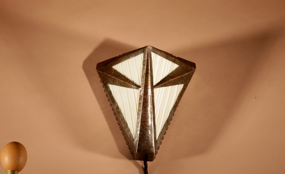 An Amsterdam School style triangular copper wall sconce featuring hand-chased geometric metalwork and pleated cream fabric panels. View V