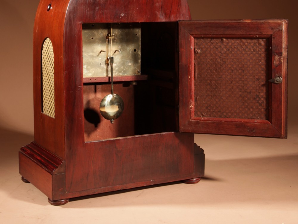 An Edwardian mahogany mantel clock featuring a pointed lancet arch top, oval marquetry inlay, and a circular white dial framed in brass. View VI