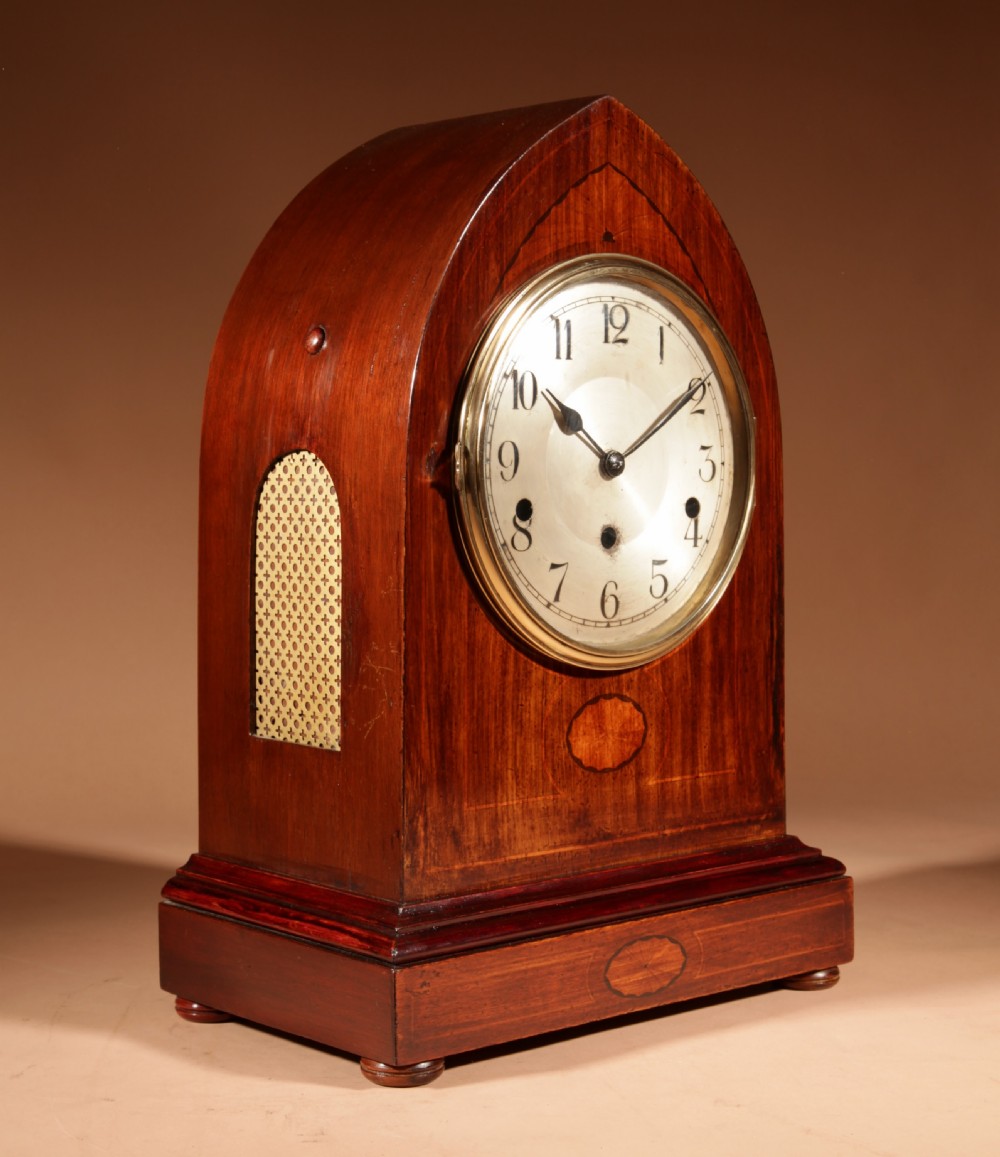 An Edwardian mahogany mantel clock featuring a pointed lancet arch top, oval marquetry inlay, and a circular white dial framed in brass. View VIII
