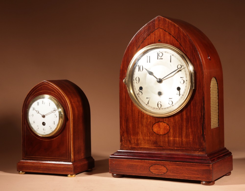 An Edwardian mahogany mantel clock featuring a pointed lancet arch top, oval marquetry inlay, and a circular white dial framed in brass. View IX