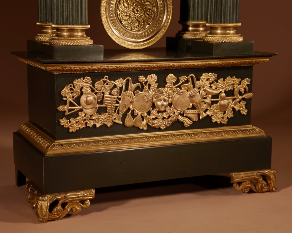 A late nineteenth-century French portico clock featuring dark patinated bronze columns, decorative gilt bronze mounts, a white enamel dial with Roman numerals, and an ornate pendulum. View II