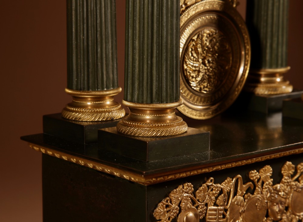 A late nineteenth-century French portico clock featuring dark patinated bronze columns, decorative gilt bronze mounts, a white enamel dial with Roman numerals, and an ornate pendulum. View VII
