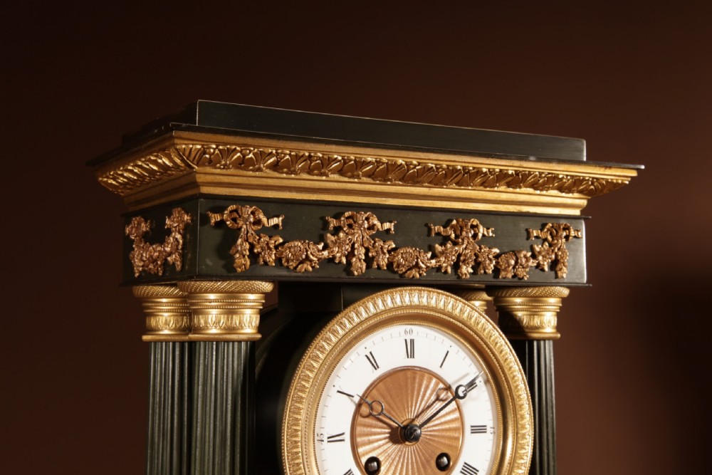 A late nineteenth-century French portico clock featuring dark patinated bronze columns, decorative gilt bronze mounts, a white enamel dial with Roman numerals, and an ornate pendulum. View VIII