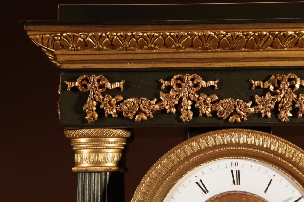 A late nineteenth-century French portico clock featuring dark patinated bronze columns, decorative gilt bronze mounts, a white enamel dial with Roman numerals, and an ornate pendulum. View IX