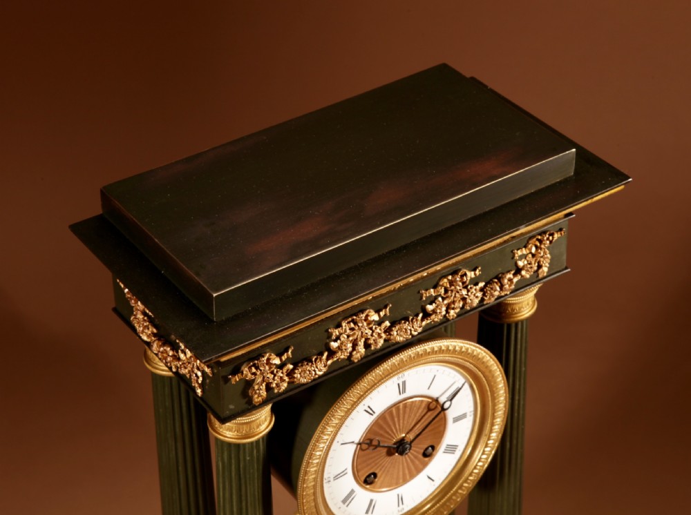 A late nineteenth-century French portico clock featuring dark patinated bronze columns, decorative gilt bronze mounts, a white enamel dial with Roman numerals, and an ornate pendulum. View XIII