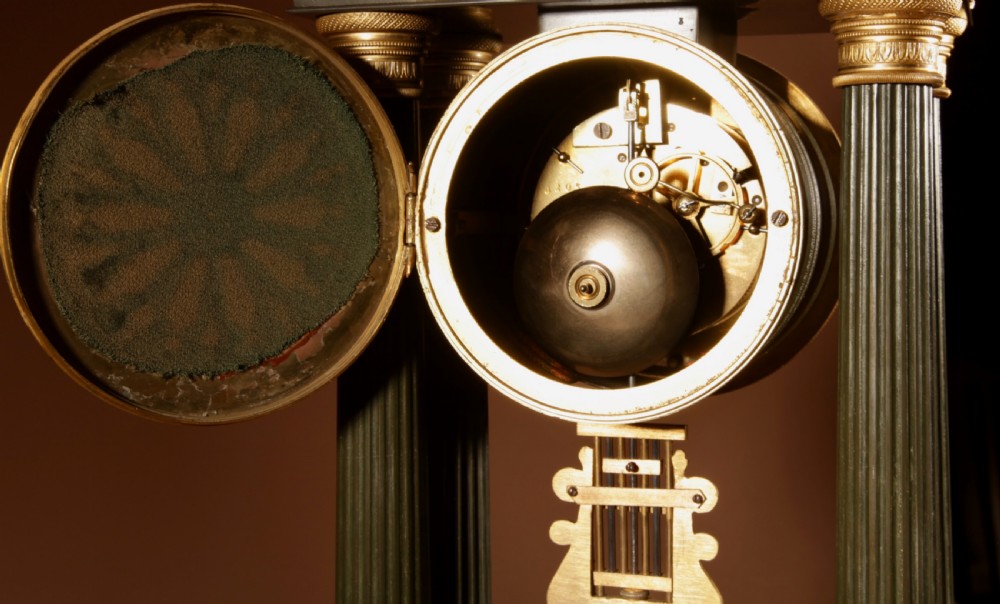 A late nineteenth-century French portico clock featuring dark patinated bronze columns, decorative gilt bronze mounts, a white enamel dial with Roman numerals, and an ornate pendulum. View XVII