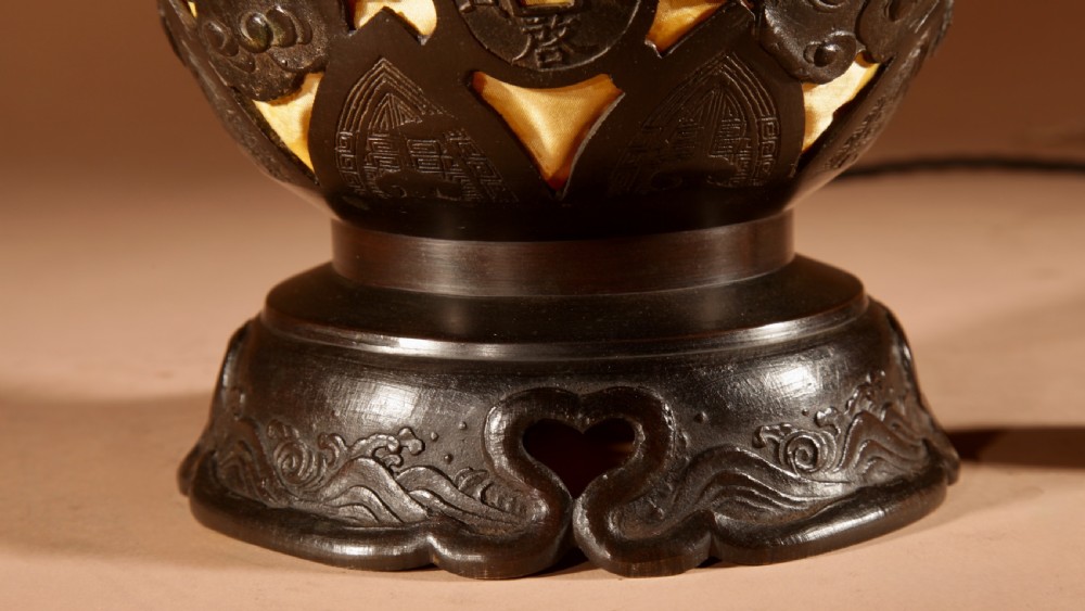 A dark bronze Japanese table lantern featuring reticulated coin and cloud pattern cut-outs, an illuminated amber interior, and a scalloped crest with a top handle. View III
