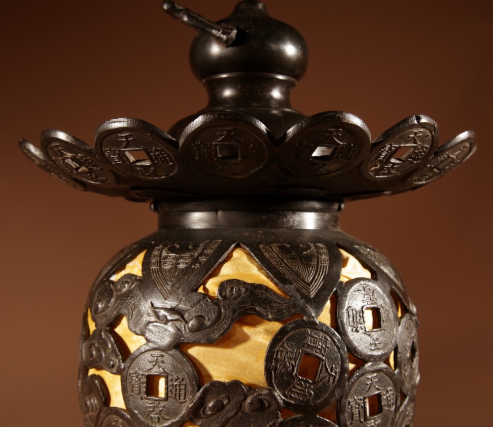 A dark bronze Japanese table lantern featuring reticulated coin and cloud pattern cut-outs, an illuminated amber interior, and a scalloped crest with a top handle. View VI