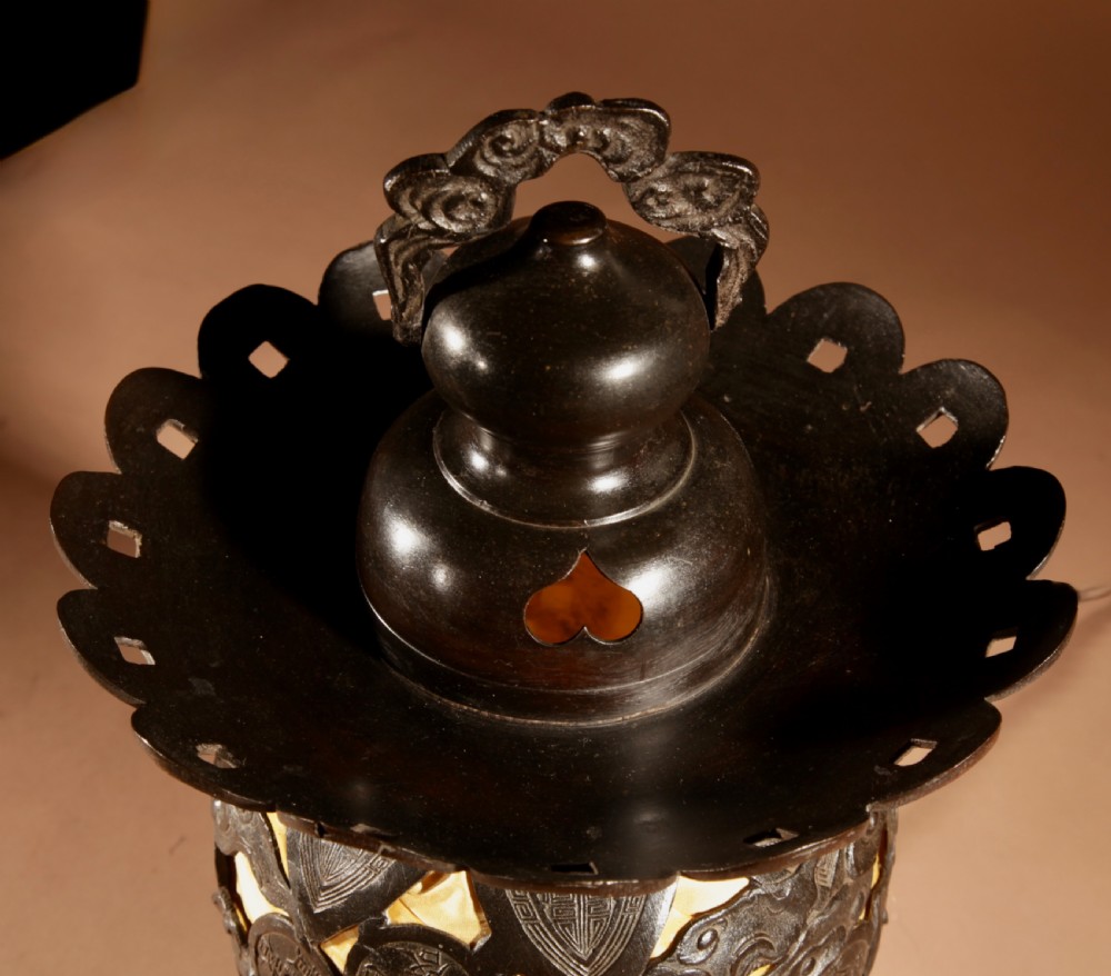 A dark bronze Japanese table lantern featuring reticulated coin and cloud pattern cut-outs, an illuminated amber interior, and a scalloped crest with a top handle. View VIII