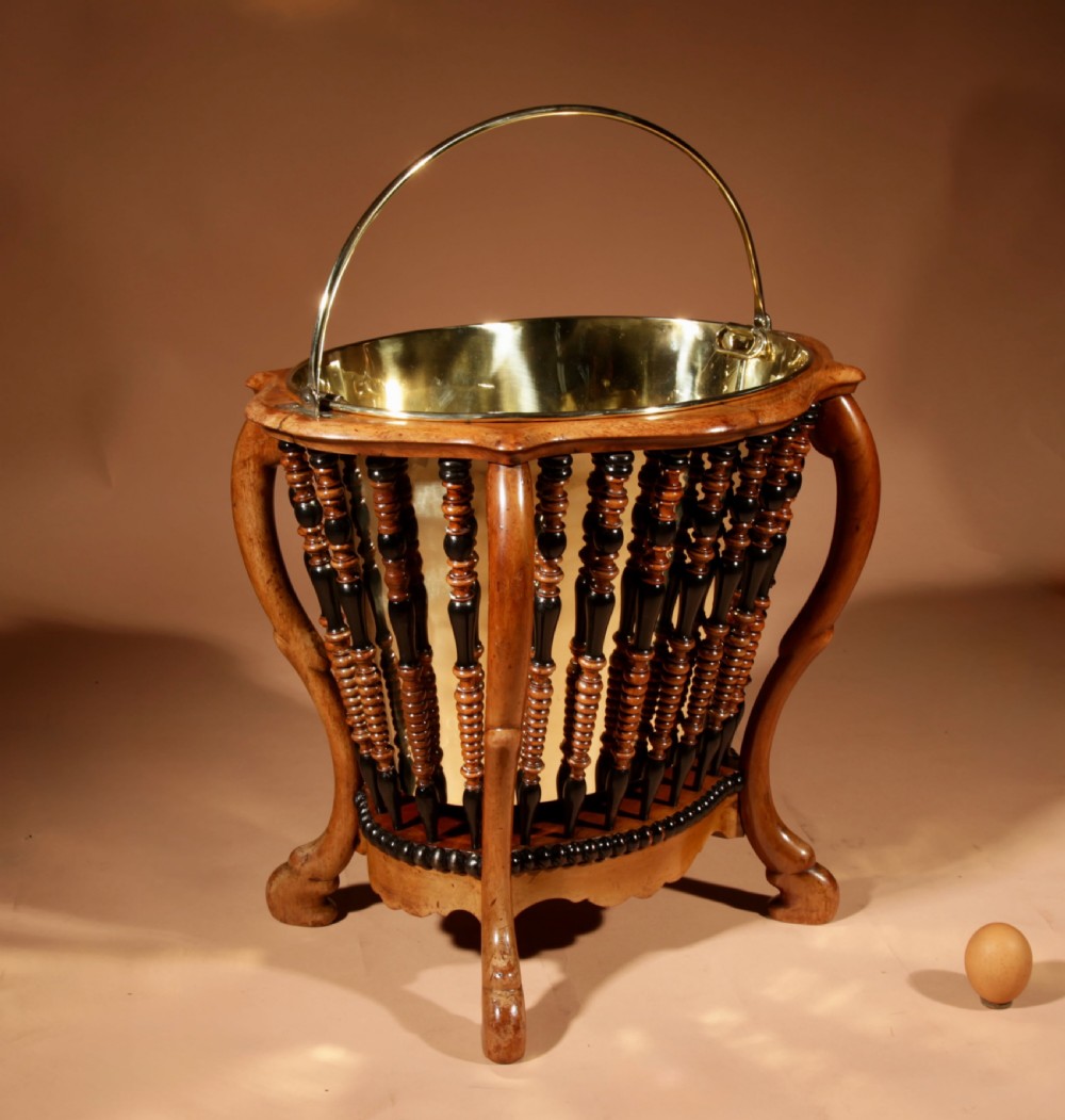 An oval Victorian walnut peat bucket featuring turned dual-tone spindles, four curved legs, and a swing-handled brass liner.