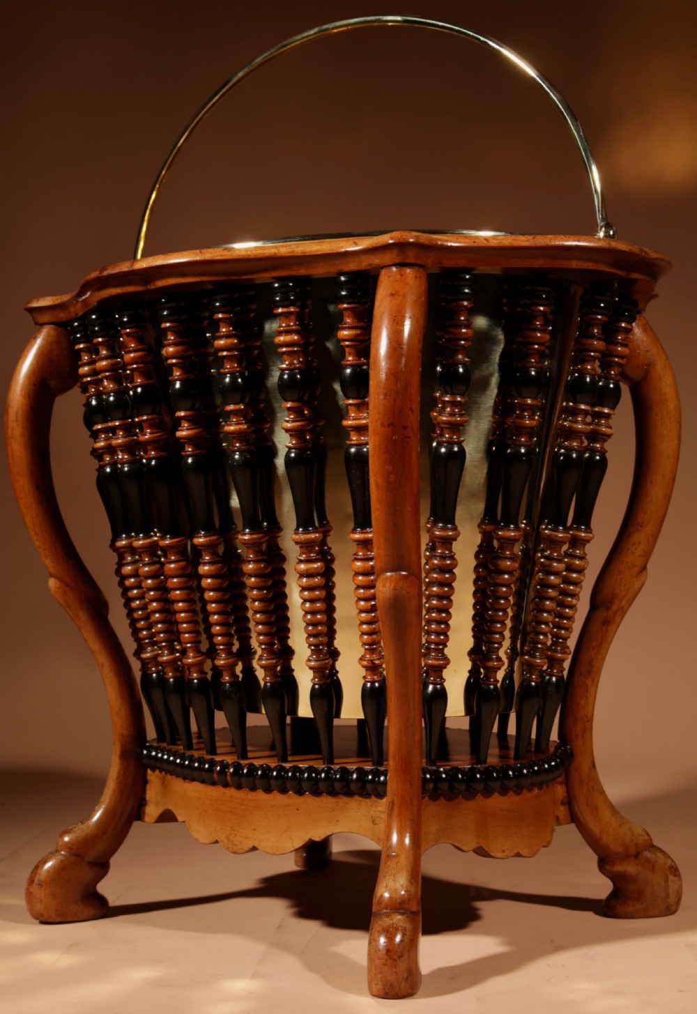 An oval Victorian walnut peat bucket featuring turned dual-tone spindles, four curved legs, and a swing-handled brass liner. View IV