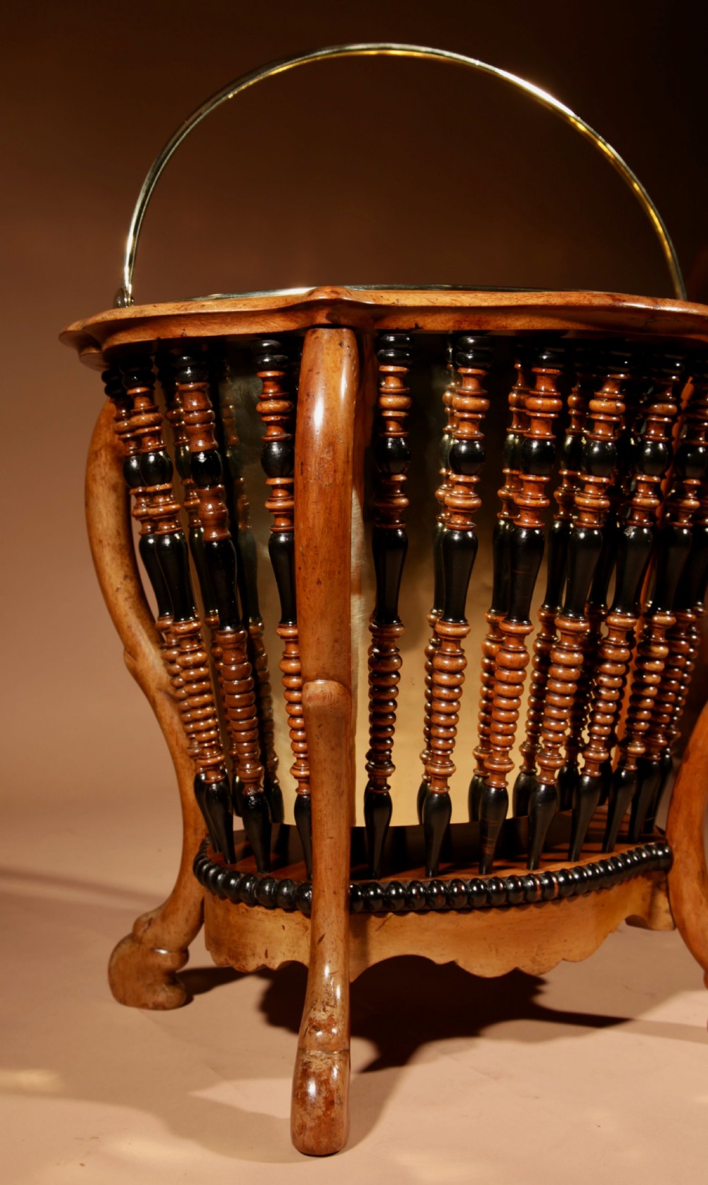 An oval Victorian walnut peat bucket featuring turned dual-tone spindles, four curved legs, and a swing-handled brass liner. View VI