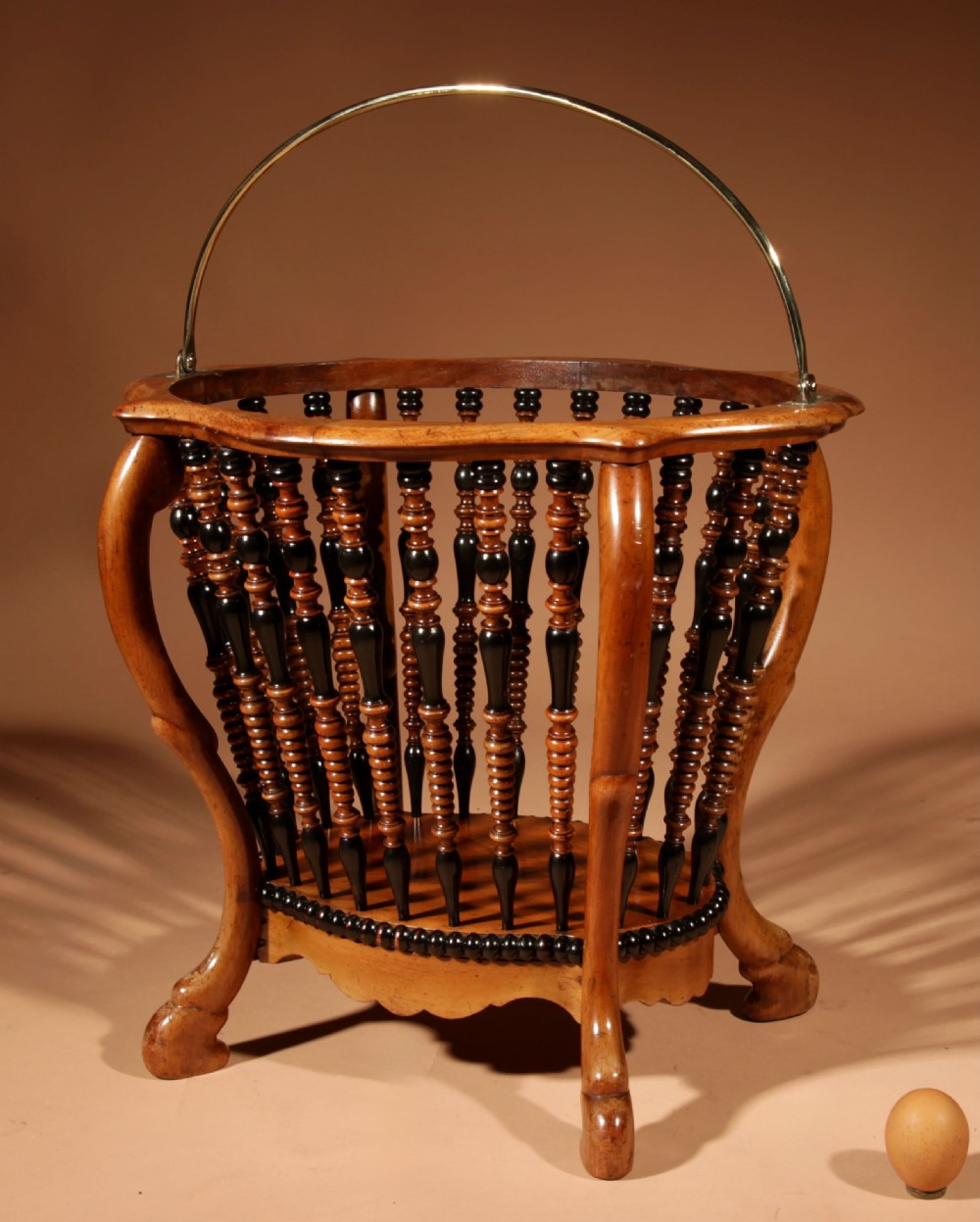 An oval Victorian walnut peat bucket featuring turned dual-tone spindles, four curved legs, and a swing-handled brass liner. View X