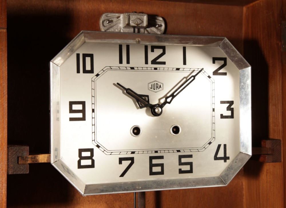A rectangular Art Deco French oak wall clock featuring stylised side carvings, a silvered octagonal-framed dial face, and an etched lower glass window revealing a metal pendulum. View II