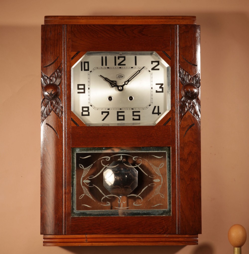 A rectangular Art Deco French oak wall clock featuring stylised side carvings, a silvered octagonal-framed dial face, and an etched lower glass window revealing a metal pendulum. View VII