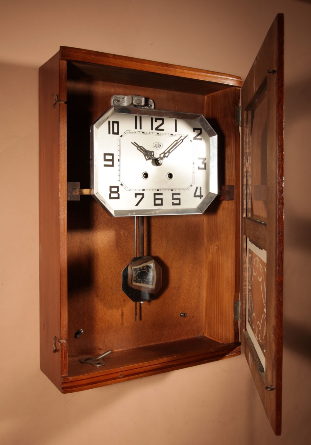 A rectangular Art Deco French oak wall clock featuring stylised side carvings, a silvered octagonal-framed dial face, and an etched lower glass window revealing a metal pendulum. View VIII