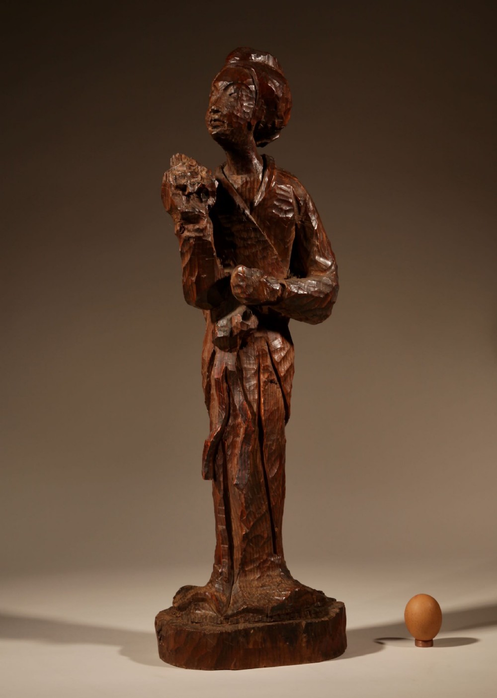 A hand-carved dark wood sculpture of a standing geisha in the Japanese nata-tsukuri style with visible chisel facets.