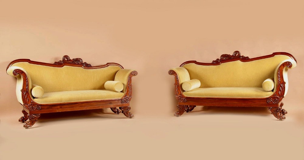 A pair of carved mahogany settees upholstered in mustard yellow velvet with cylindrical bolster cushions.