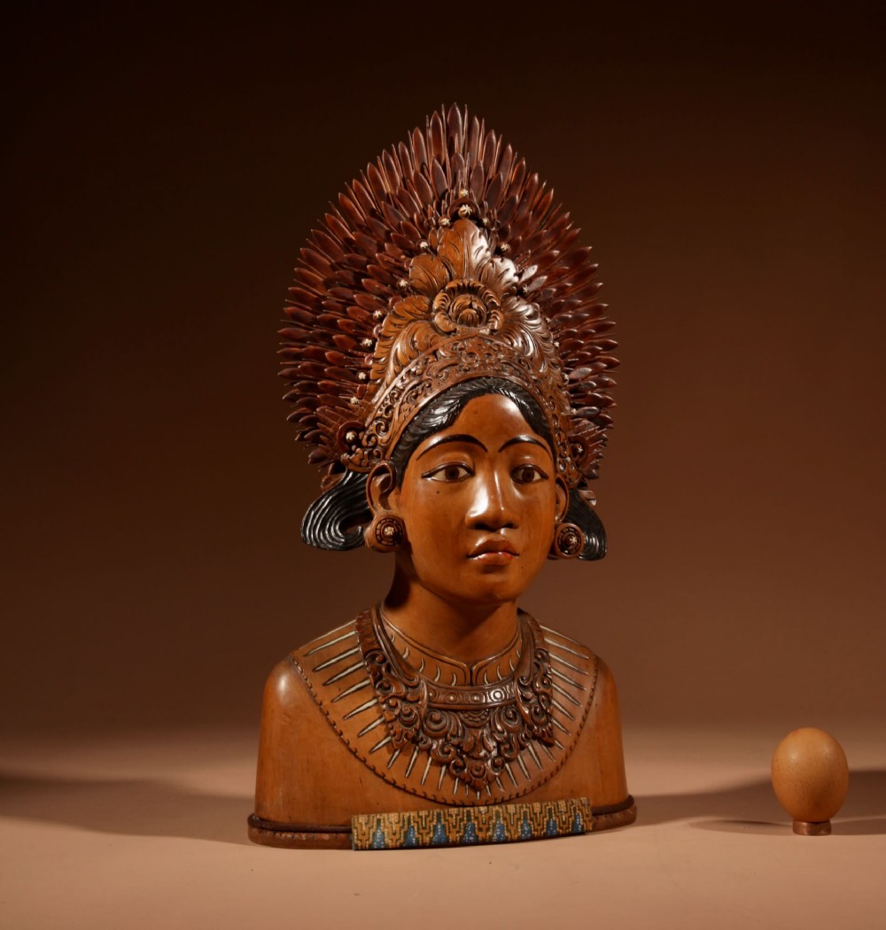 A carved wooden bust depicting an Indonesian Janger dancer with a detailed spiked fan headdress, ornate painted collar, and expressive facial features.