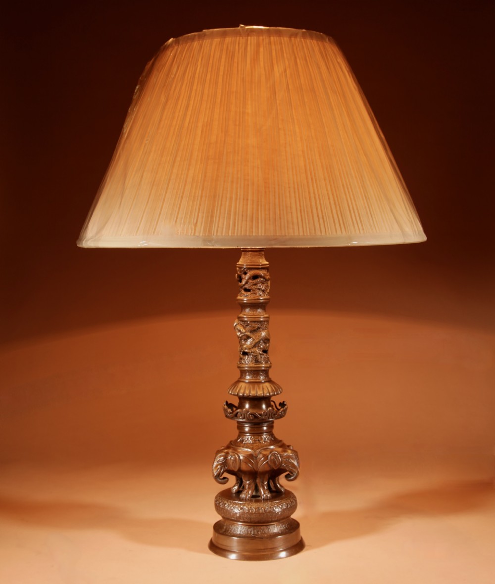A dark patinated bronze table lamp featuring cast elephant and dragon motifs topped with a pleated conical lampshade.