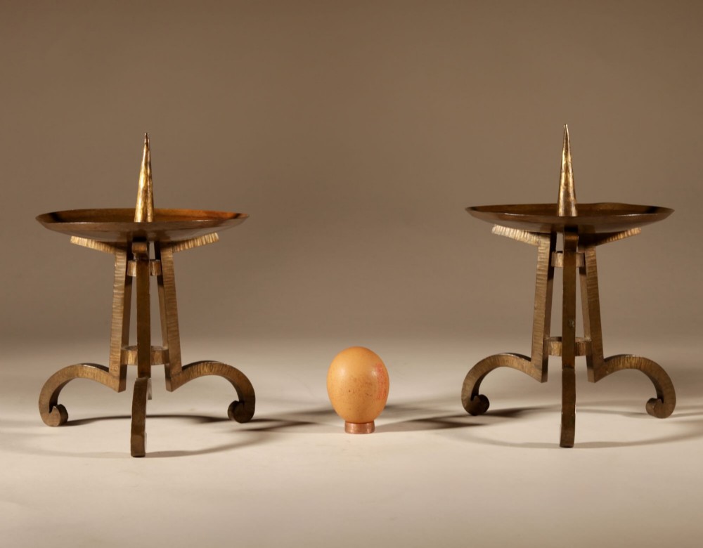 A pair of hand-wrought brass pricket candlesticks featuring hammered tripod legs, scrolled feet, dished drip pans, and upright central spikes.