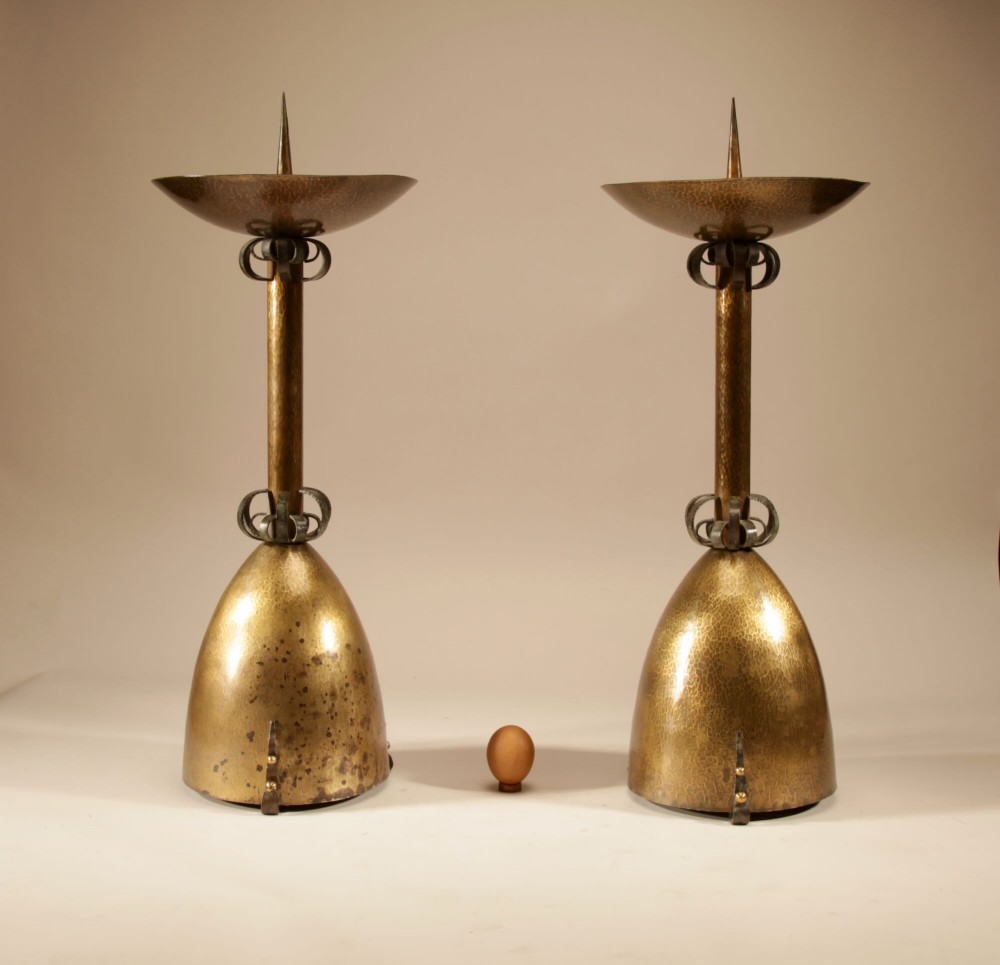 A pair of tall hand-hammered brass pricket candlesticks featuring bell-shaped bases and openwork wrought iron scroll collars.