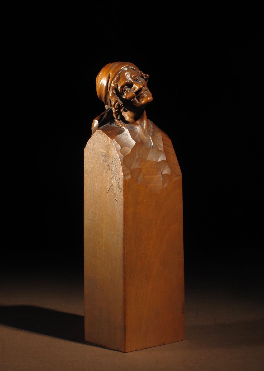 Hand-carved pearwood sculpture of an elderly woman wearing a headscarf, emerging from an integral tall rectangular pedestal signed by Hermann Steiner Meran.