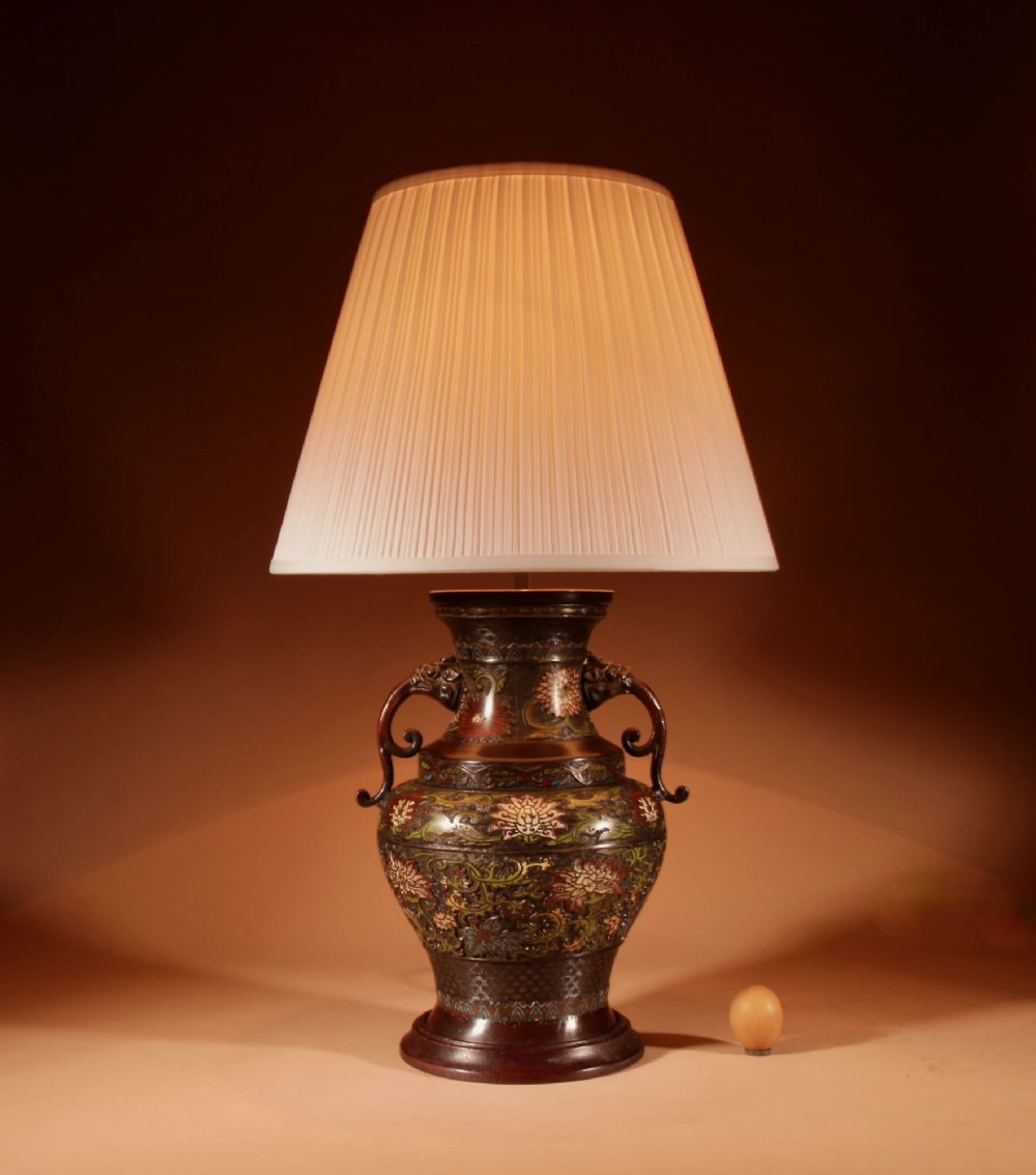 A Japanese champleve bronze table lamp featuring floral enamel decoration, twin side handles, and a cream pleated shade.