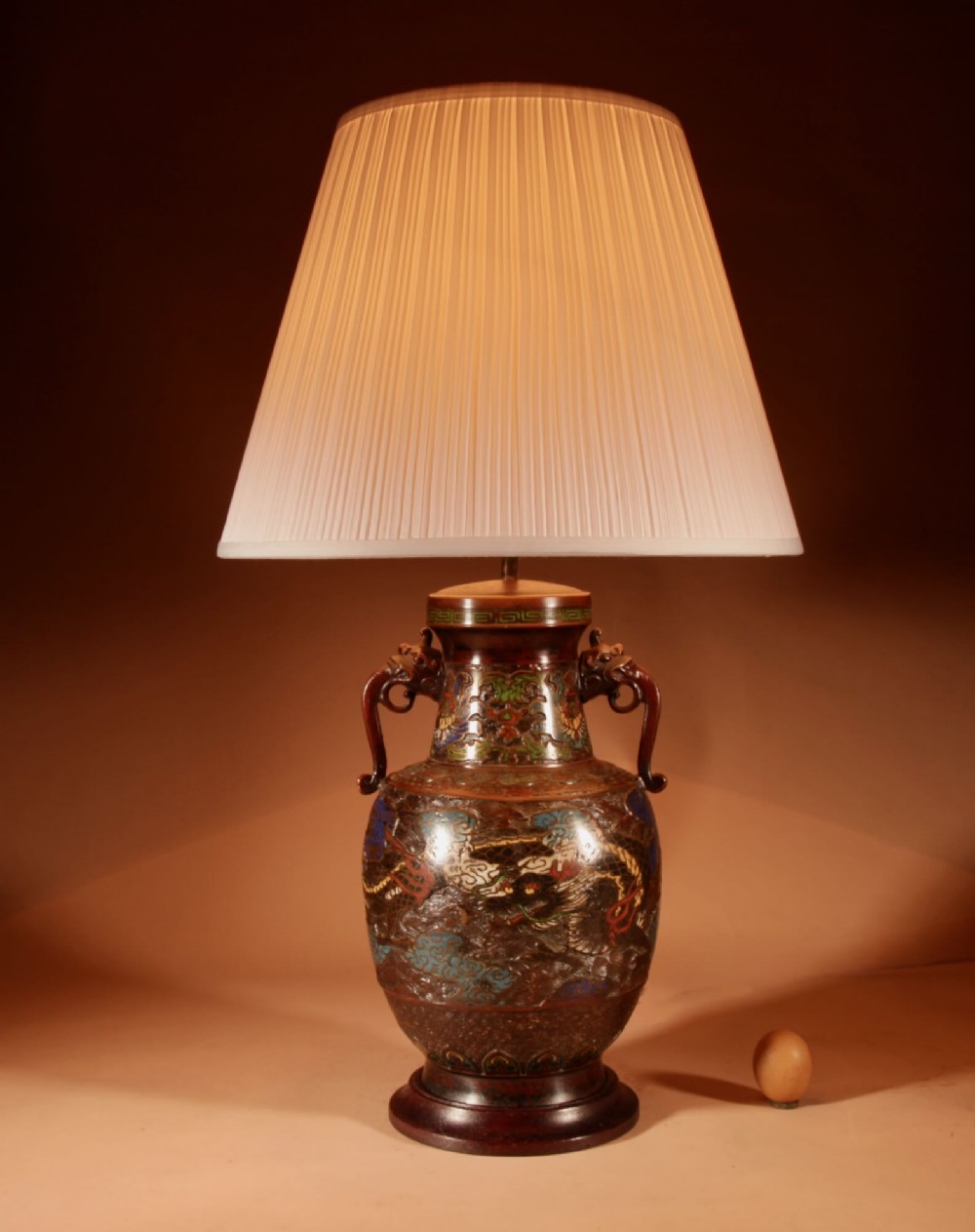 An antique Japanese champleve bronze vase converted into a table lamp, featuring dragon motifs, twin handles, colourful enamel inlay, and topped with a pleated cream lampshade.