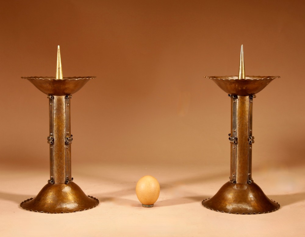 A pair of patinated brass pricket candlesticks featuring hand-hammered scalloped bases, riveted cylindrical shafts, and central spikes.