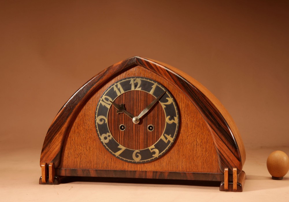 An Amsterdam School mantel clock featuring an arched oak case framed with dark Macassar ebony trim and a circular dial with brass numbers.