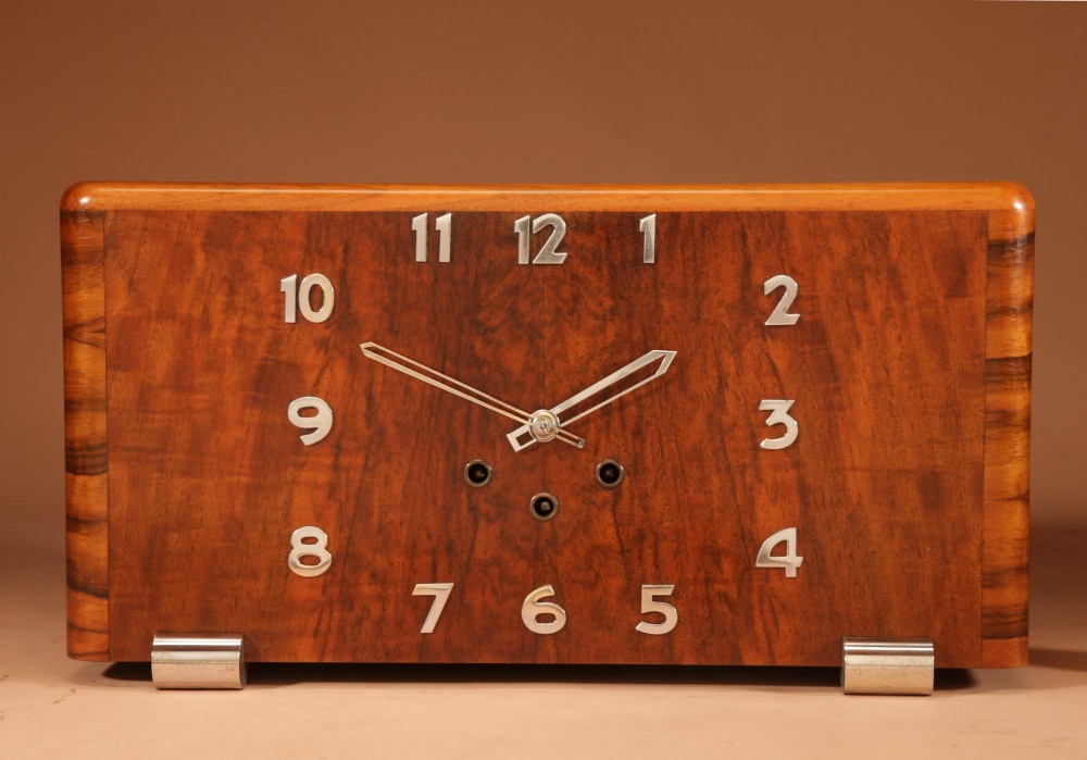 A rectangular French Art Deco mantel clock crafted from figured walnut veneer featuring applied chrome numerals, geometric hands, and chrome bracket feet.