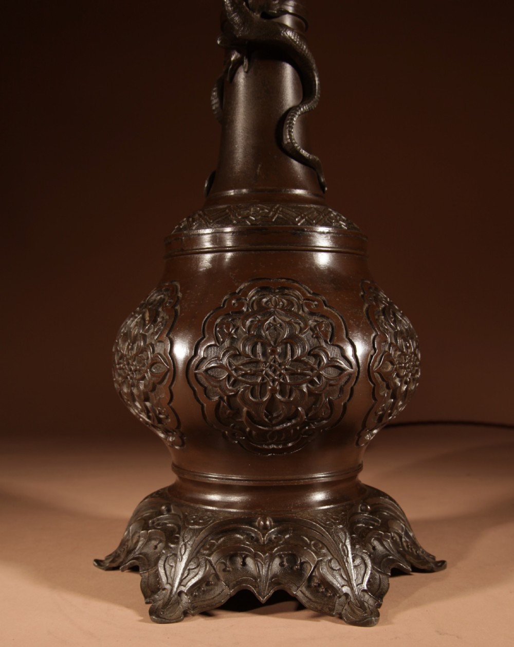 A dark patinated metal table lamp with relief dragon decoration, fitted with a pleated flared lampshade. View II