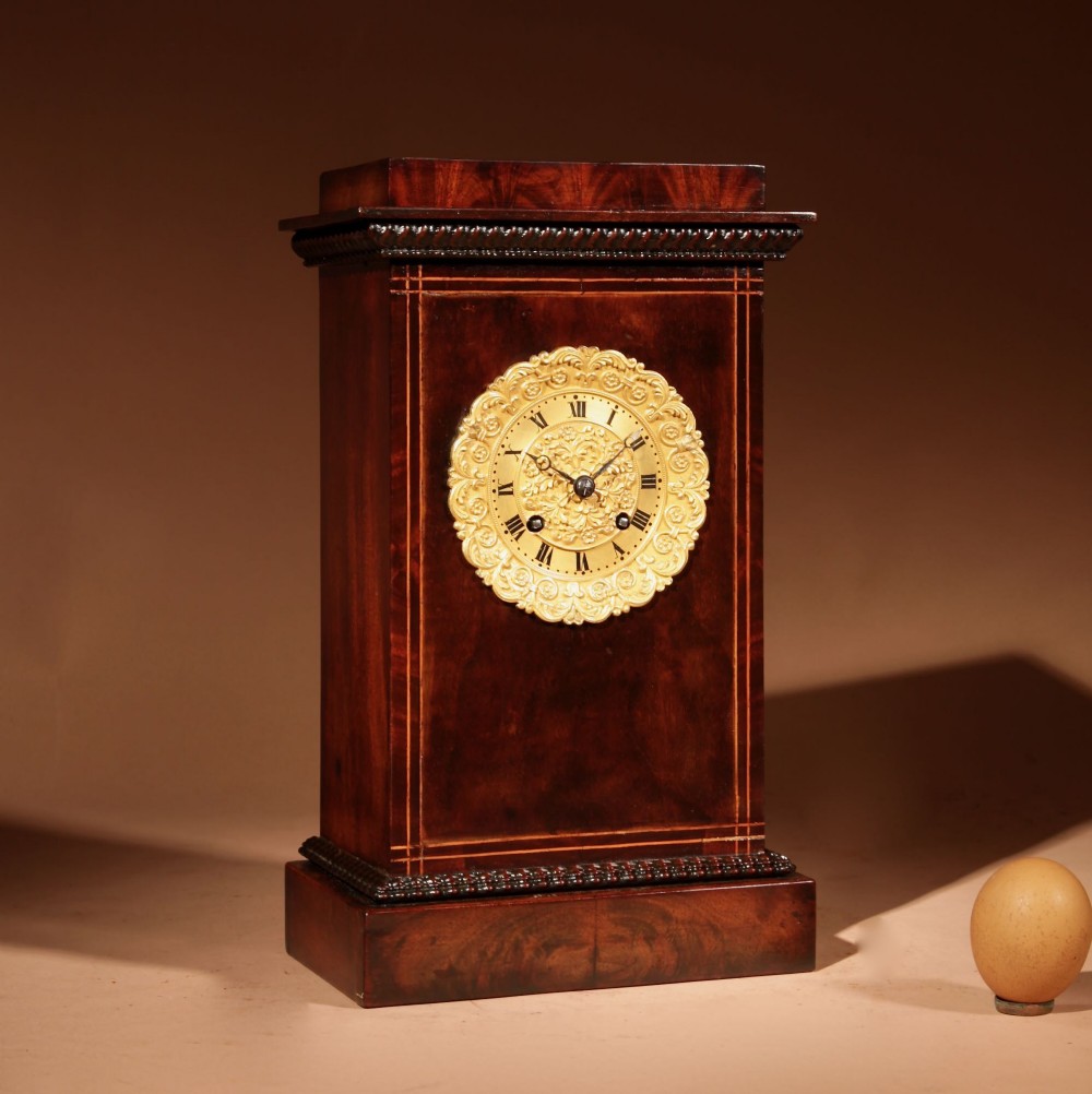 A rectangular French Louis Philippe mantel clock featuring deep mahogany veneer, boxwood inlay, carved rope twist mouldings, and a central circular gilded brass dial with Roman numerals.