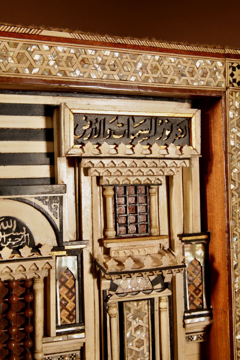 A framed three-dimensional wooden relief diorama depicting a Moorish building facade with intricate mother-of-pearl geometric inlay, miniature lattice windows, and Arabic calligraphy. View III
