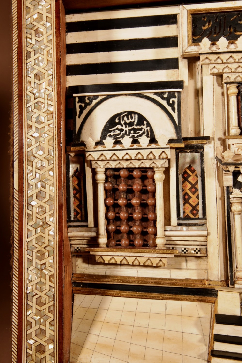 A framed three-dimensional wooden relief diorama depicting a Moorish building facade with intricate mother-of-pearl geometric inlay, miniature lattice windows, and Arabic calligraphy. View IV