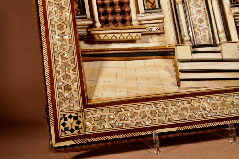 A framed three-dimensional wooden relief diorama depicting a Moorish building facade with intricate mother-of-pearl geometric inlay, miniature lattice windows, and Arabic calligraphy. View V