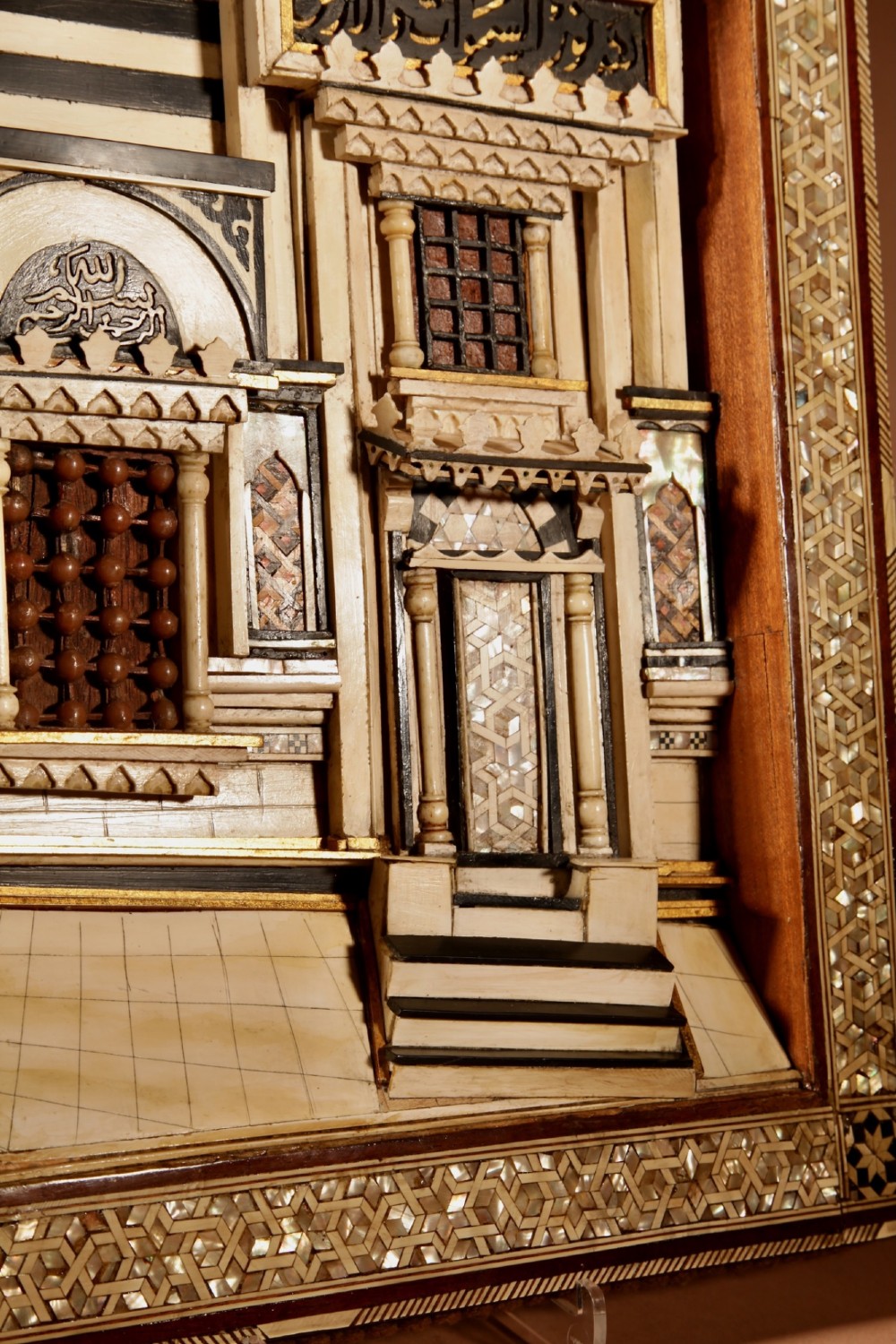 A framed three-dimensional wooden relief diorama depicting a Moorish building facade with intricate mother-of-pearl geometric inlay, miniature lattice windows, and Arabic calligraphy. View VII