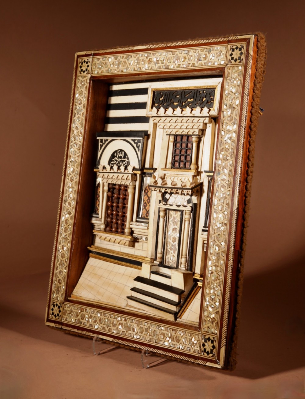 A framed three-dimensional wooden relief diorama depicting a Moorish building facade with intricate mother-of-pearl geometric inlay, miniature lattice windows, and Arabic calligraphy. View VIII