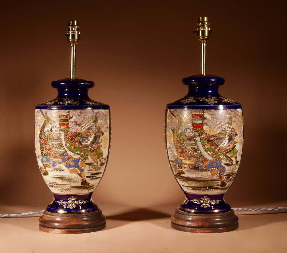A pair of Japanese Satsuma ceramic table lamps featuring hand-painted figure scenes, cobalt blue accents, dark wooden bases, and cream pleated lampshades. View II