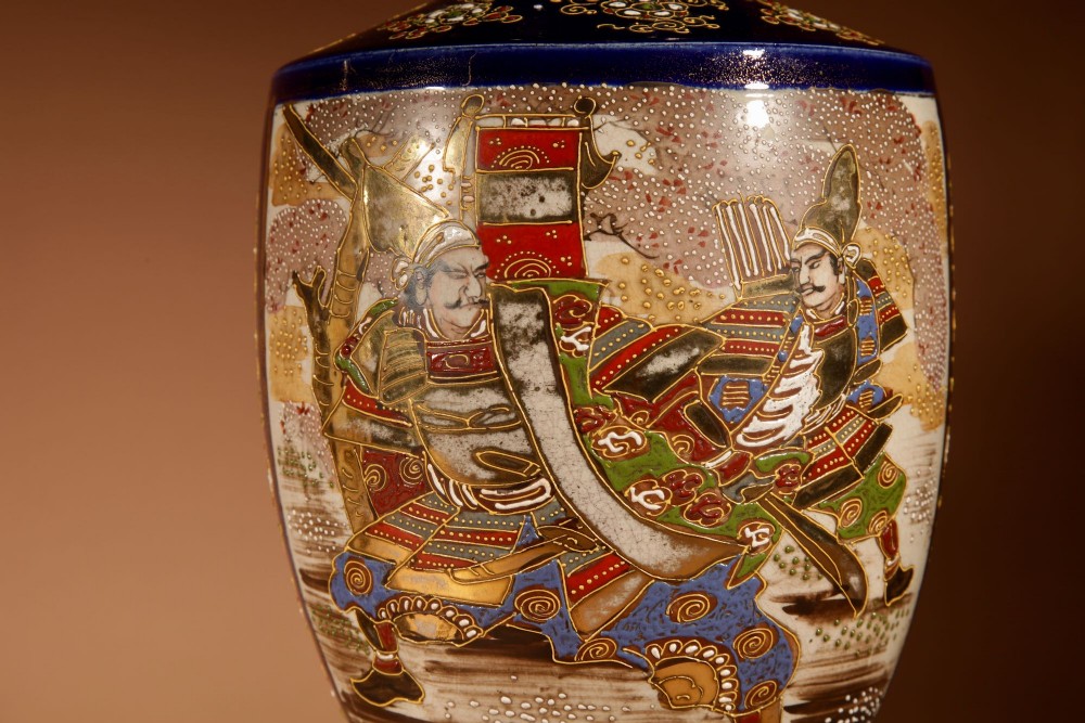 A pair of Japanese Satsuma ceramic table lamps featuring hand-painted figure scenes, cobalt blue accents, dark wooden bases, and cream pleated lampshades. View III