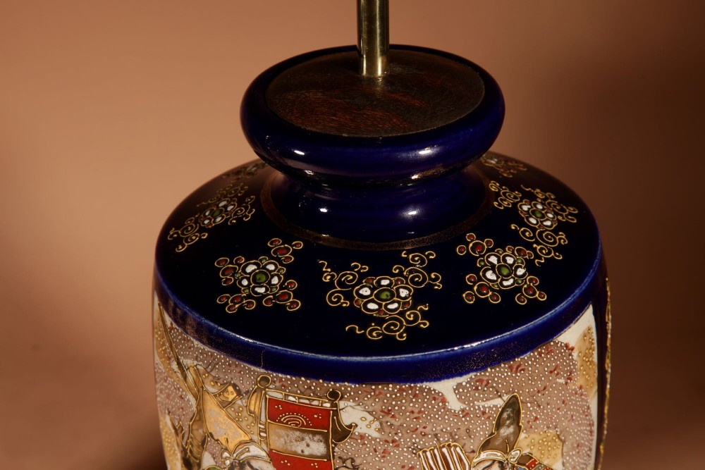 A pair of Japanese Satsuma ceramic table lamps featuring hand-painted figure scenes, cobalt blue accents, dark wooden bases, and cream pleated lampshades. View V