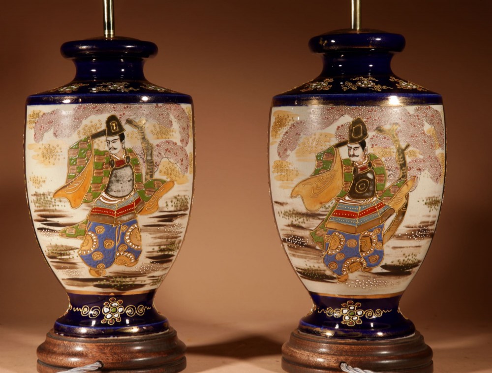 A pair of Japanese Satsuma ceramic table lamps featuring hand-painted figure scenes, cobalt blue accents, dark wooden bases, and cream pleated lampshades. View VI