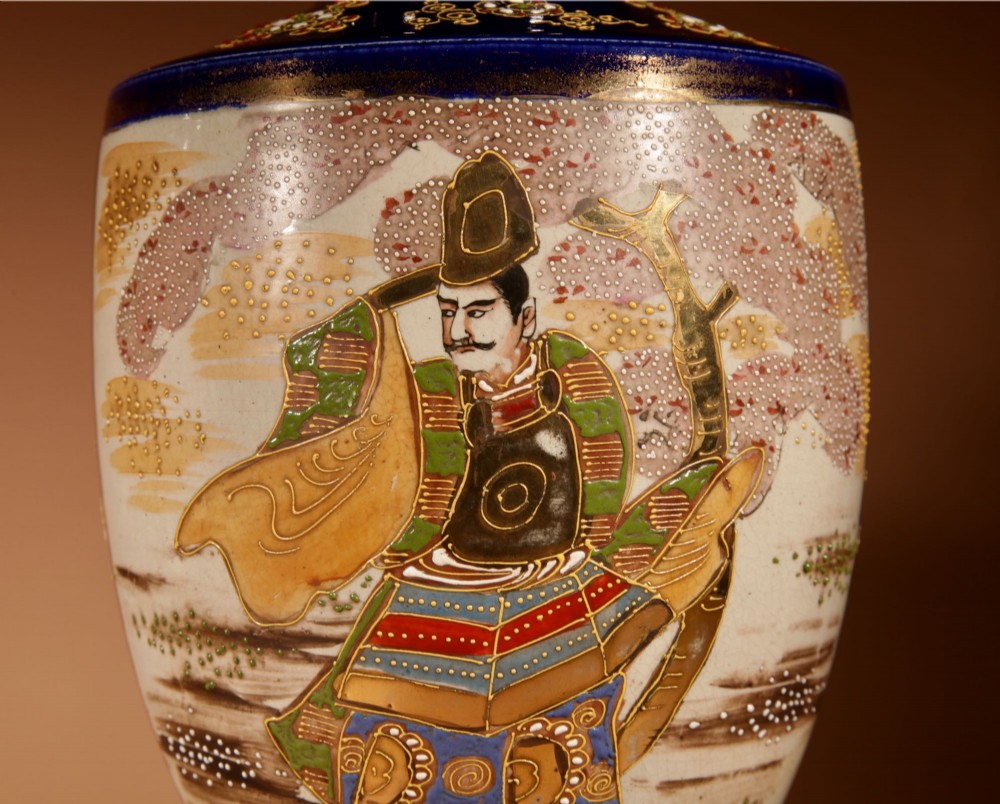 A pair of Japanese Satsuma ceramic table lamps featuring hand-painted figure scenes, cobalt blue accents, dark wooden bases, and cream pleated lampshades. View VII
