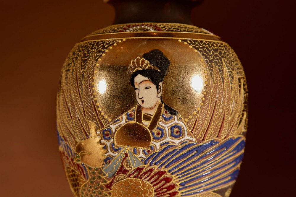 A pair of small Japanese Satsuma ceramic table lamps featuring figure paintings, gold gilding, dark wooden bases, and pleated cream shades. View IV