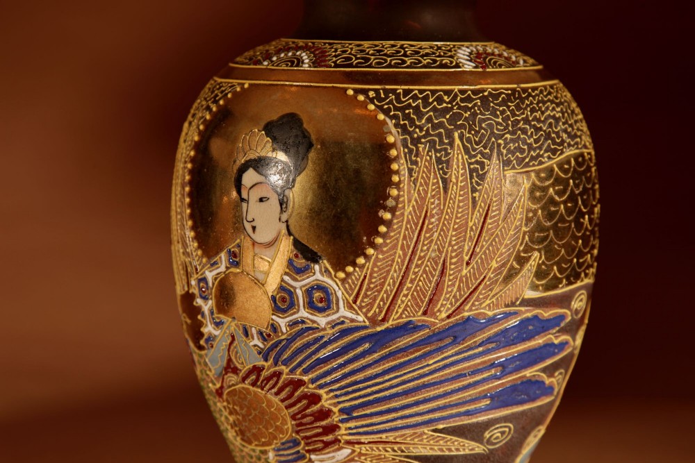 A pair of small Japanese Satsuma ceramic table lamps featuring figure paintings, gold gilding, dark wooden bases, and pleated cream shades. View V