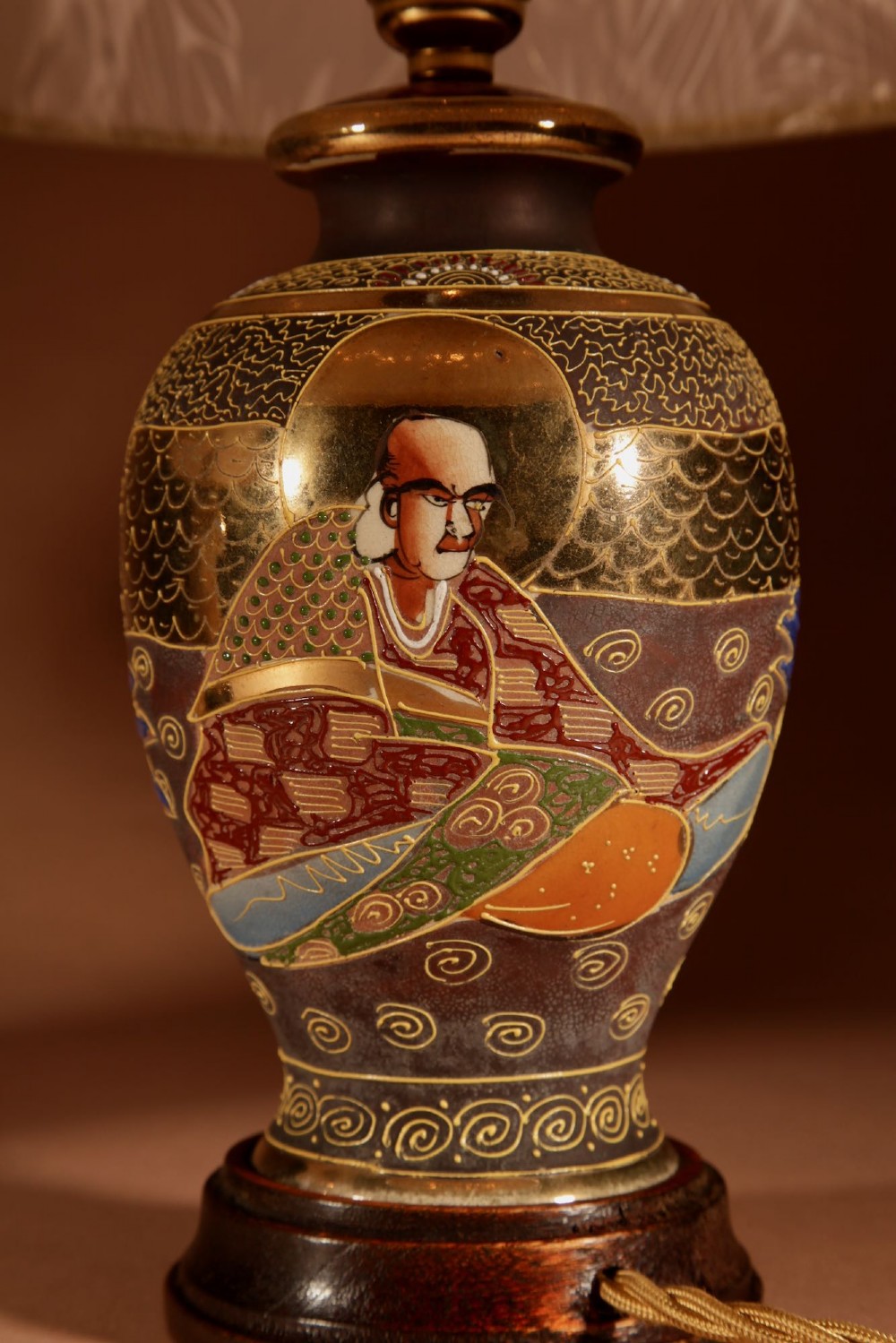 A pair of small Japanese Satsuma ceramic table lamps featuring figure paintings, gold gilding, dark wooden bases, and pleated cream shades. View VI