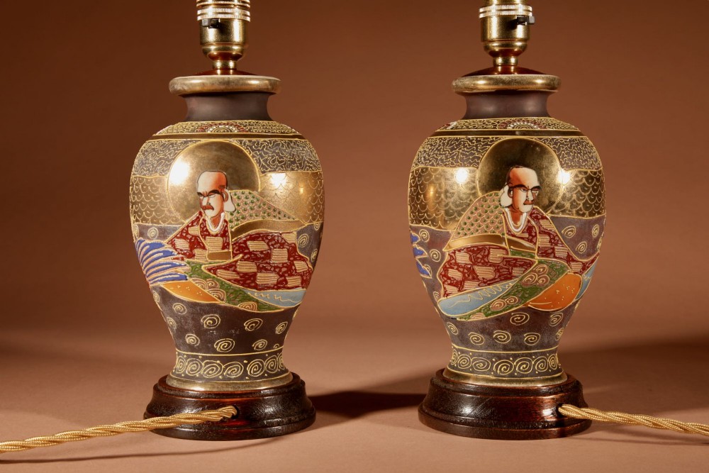 A pair of small Japanese Satsuma ceramic table lamps featuring figure paintings, gold gilding, dark wooden bases, and pleated cream shades. View VIII